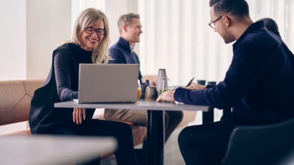 Four people sitting on a table in a meeting room in front of a window