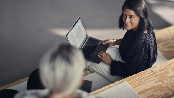 Zwei Frauen sitzen auf einer Treppe, eine hat einen Laptop auf ihrem Schoss