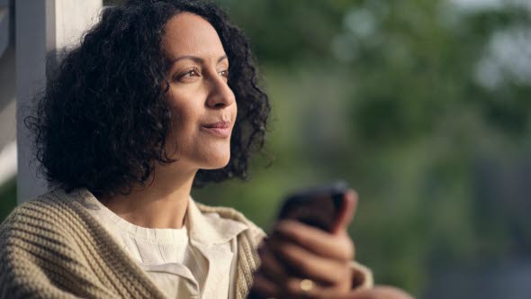 Frau sitzt am Fenster mit Handy