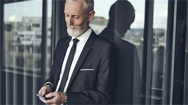 Mann der vor einem Fenster steht und auf sein Mobiltelefon schaut