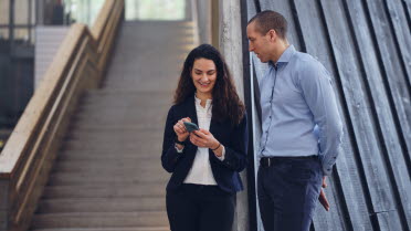 Mann und Frau stehen vor einer Treppe und schauen auf ihr Mobiltelefon