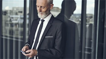 Mann steht am Fenster und schaut auf sein Mobiltelefon