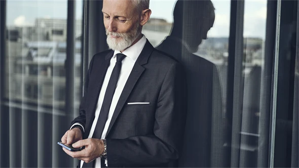 Mann steht am Fenster und schaut auf sein Smartphone