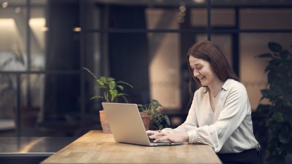 Frau sitzt an Tisch mit Laptop und tippt