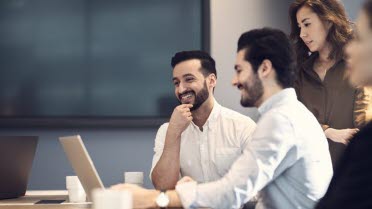 Zwei Personen sitzen um einen Laptop und diskutieren. Zwei Personen stehen dahinter.